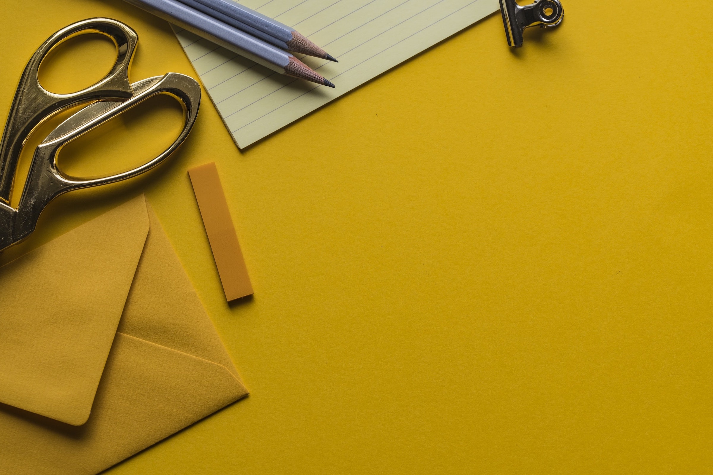 A yellow background with envelopes, notepads, folder tabs, pencils, and scissors set on top