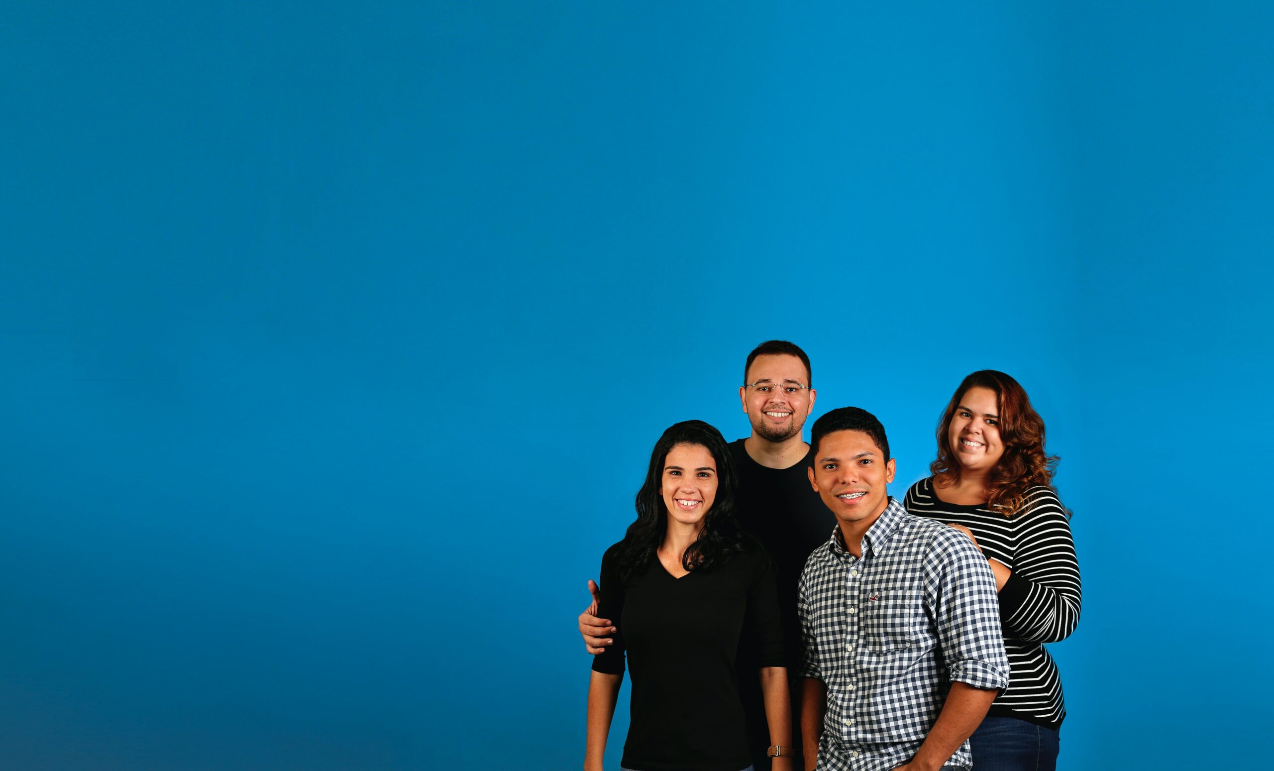 A mixed gender and ethnicity group of young employees in various work appropriate attire standing in front of a Goodwill blue background